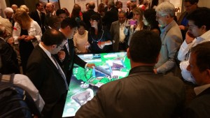 A crowd of people surrounds the 84-inch multitouch table displaying a 3D model of Cusco.